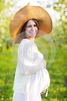 Pregnant woman wearing big hat and white dress in blooming garde