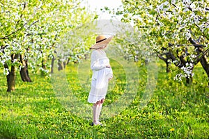 Pregnant woman wearing big hat and white dress in blooming garden