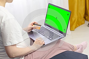 Pregnant woman wearing casual clothes hands holding credit card and laptop with mockup green blank display