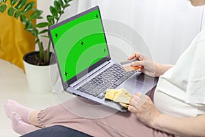 Pregnant woman wearing casual clothes hands holding credit card and laptop with mockup green blank display