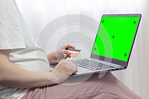 Pregnant woman wearing casual clothes hands holding credit card and laptop with mockup green blank display