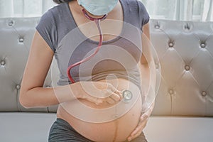 A pregnant woman wears a surgical mask and checking her fetus by stethoscope. Protect a COVID-19 Coronavirus, PM 2.5 and prevent