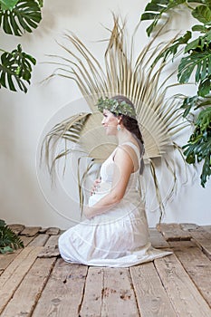 Pregnant woman in white dress holds hands on belly. Pregnancy, maternity, preparation and expectation concept.