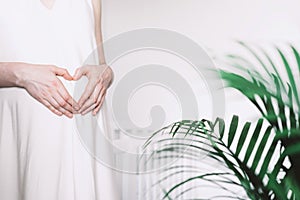 Pregnant woman in white dress making heart on pregnant belly. Maternity, preparation for childbirth, baby