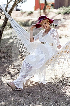 Pregnant woman in white dress resting on outdoor hammock