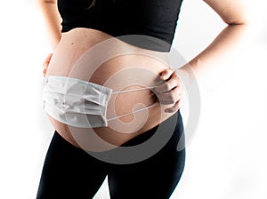 Pregnant woman white medicinal face mask on her pregnant belly abdomen. Coronavirus covid19