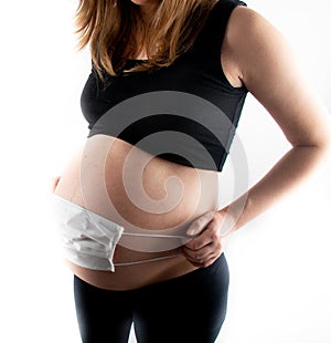 Pregnant woman white medicinal face mask on her pregnant belly abdomen. Coronavirus covid19