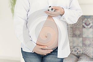 A pregnant woman in a white shirt holds her hands on the belly.