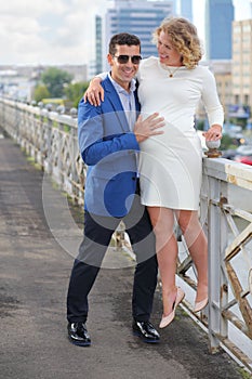 Pregnant woman in white stands on railings and photo