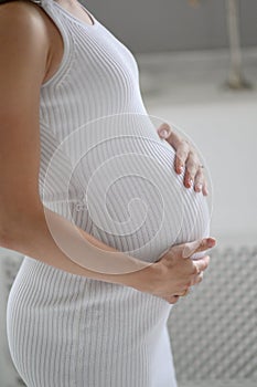 Pregnant woman in white sweater holding her belly.  close up of happy pregnant