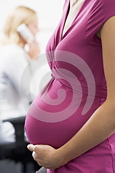 Pregnant woman at work holding belly with coworker