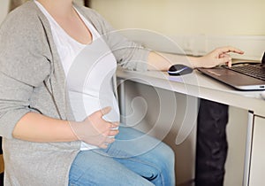 Pregnant woman working on laptop at her working place in office. Medical insurance childbearing. Maternity leave. Pregnancy and