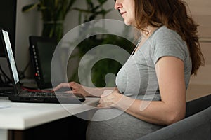 A pregnant woman is working on a laptop. Work during pregnancy from home.