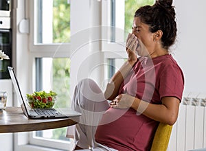 Pregnant woman working on laptop and yawning at home