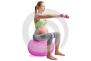 Pregnant woman working out on medicine ball with dumbells in hands