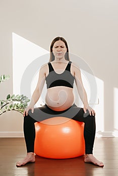 A pregnant woman is writhing in pain exhaling air with her arms on her knees