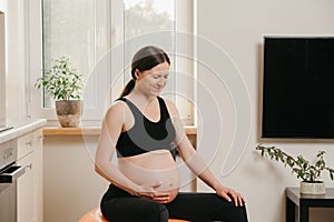A pregnant woman is writhing in pain with her arm on belly on an exercise ball