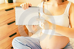 Pregnant woman writing list. Young pregnancy mother holding notepad. Pregnant lady writing check list of baby. Concept