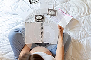 Pregnant woman writing list. Young pregnancy mother holding notepad. Pregnant lady writing check list of baby. Concept