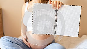 Pregnant woman writing list. Young pregnancy mother holding notepad. Pregnant lady writing check list of baby. Concept