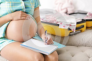 Pregnant woman writing packing list for maternity hospital at home
