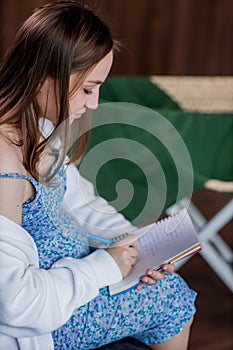 Pregnant woman writing packing list for maternity hospital at home, closeup.