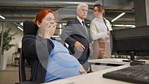 Pregnant woman yawns at work. Colleagues look disapprovingly.
