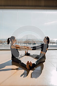 Pregnant woman and yoga instructor stretching in the morning sunlight at fitness center