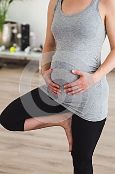 Pregnant woman doing prenatal yoga standing in tree pose