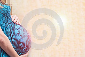 Pregnant womans belly on a light background. Sun glare effect. Copy space