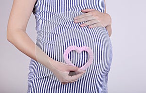 Pregnant women holding heart symbol placed on belly on grey background