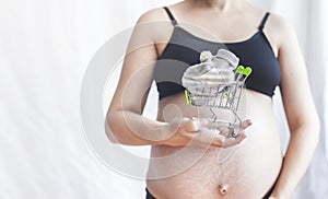 Pregnant women holding shopping cart with baby shoes. Pregnancy shopping item for kid concept