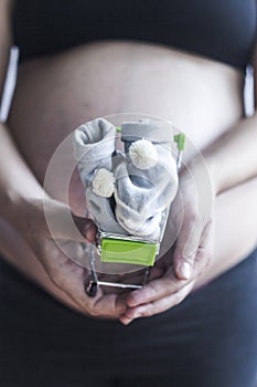 Pregnant women holding shopping cart with baby shoes. Pregnancy shopping item