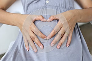 Pregnant women put her hand on her belly to heart shape.