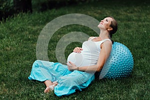 Pregnant yoga prenatal doing different exercises with fitball. in park on the grass, breathing, stretching, Pilates.