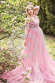 Pregnant young beautiful woman in pink lace long dress in a flowering garden