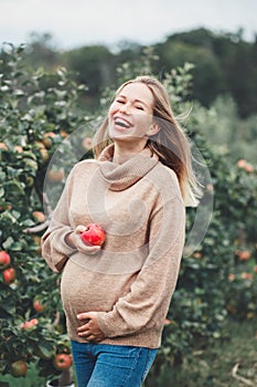 Pregnant young blonde Caucasian woman on apple farm with wicker basket