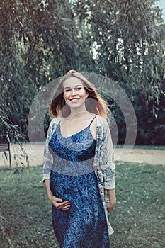 pregnant young Caucasian woman wearing long blue dress posing in park outside.