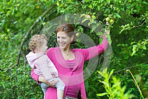 Pregnant young mother and her baby daughter in apple garden