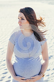 Pregnant young mother to be, standing outdoors looking away, beach scene