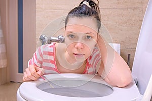 Pregnant young tired woman is vomiting in toilet sitting on the floor at home and looking at camera.