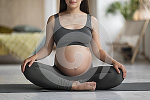 Pregnant Young Woman In Activewear Sitting On Yoga Mat At Home, Cropped