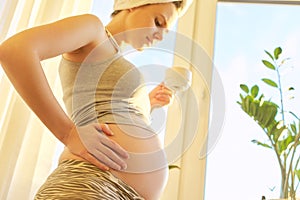 Pregnant young woman with bath towel on head with cup of tea looking out window