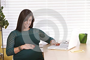 Pregnant young woman at desk looking at belly