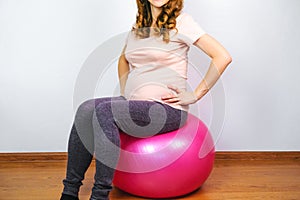 Pregnant young woman doing exercises sitting on fit ball. Active pregnancy and maternity fitness.