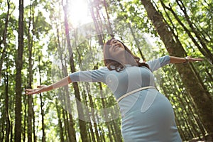 Pregnant young woman enjoying the forest with open arms