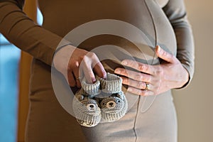 Pregnant young woman with hands touching the belly and holding baby shoes