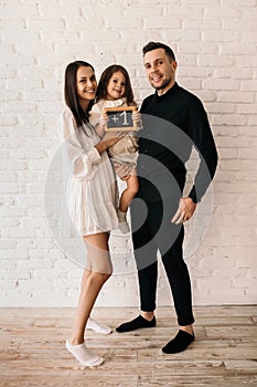 Pregnant young woman, her husband and daughter posing on a white background