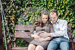 A pregnant young woman and her husband. A happy family sitting on a swing, holding belly. pregnant woman relaxing in the park.