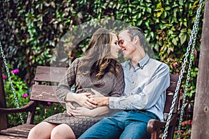 A pregnant young woman and her husband. A happy family sitting on a swing, holding belly. pregnant woman relaxing in the park.